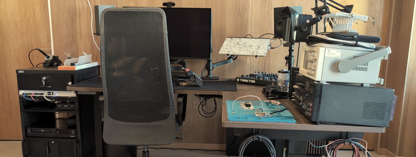 The studio bench: monitor, oscilloscope, a board under test on the soldering mat, cables below the desk